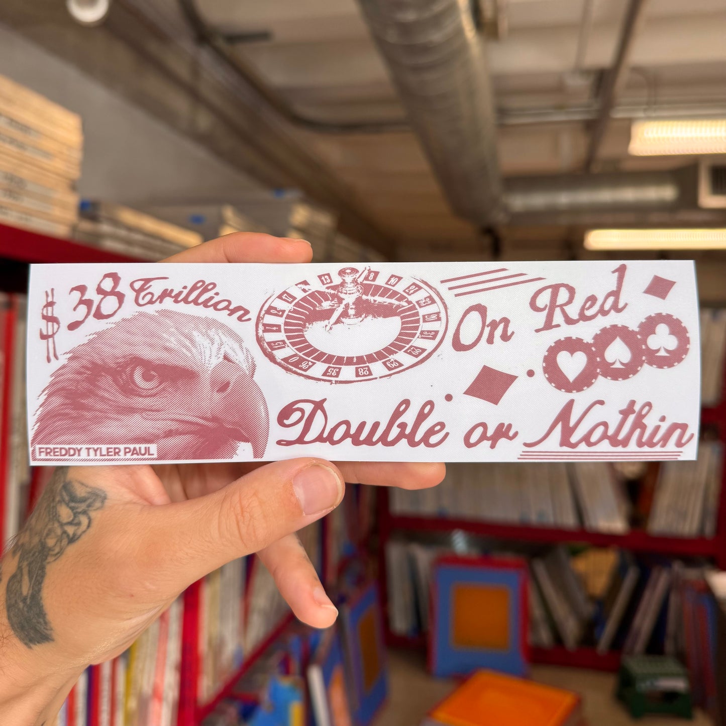 Hand holding a red and white card with an eagle design and text in a room with bookshelves.