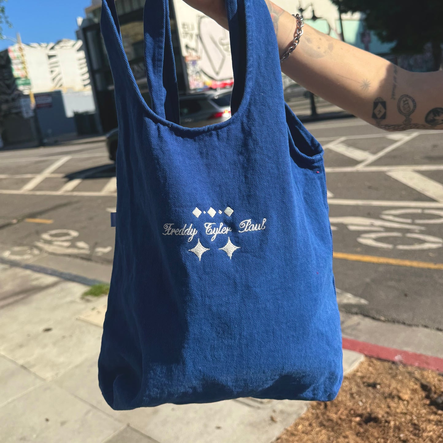 Blue tote bag with branding held by a person on a city street.