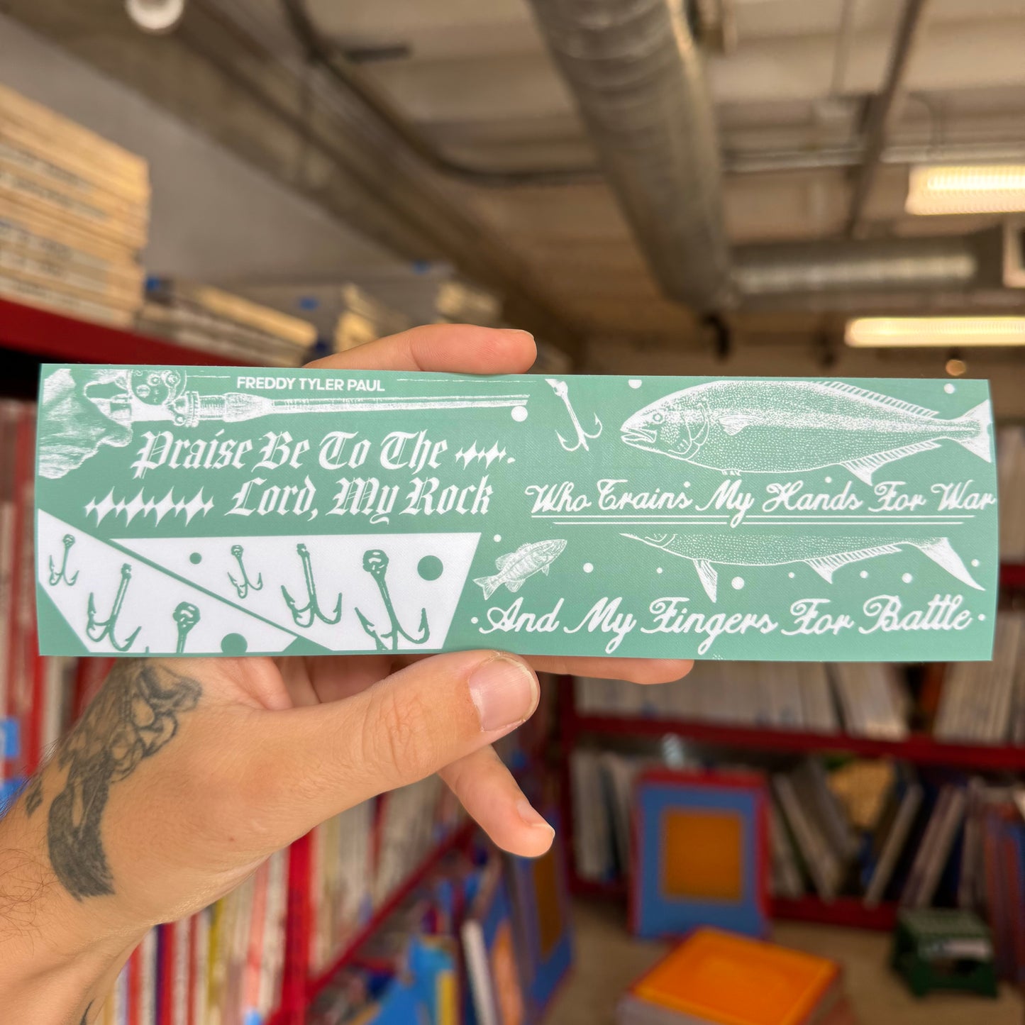 Hand holding a green and white bookmark with text and illustrations in a bookstore setting.