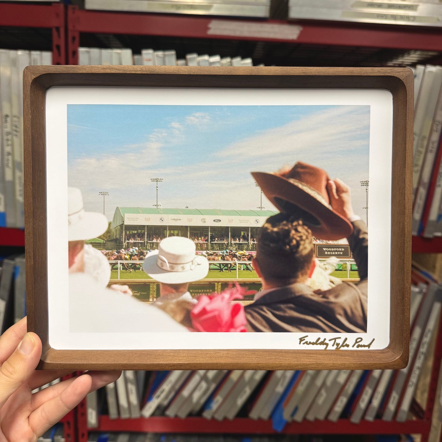 Framed photograph of people at a sports event held by a hand in a warehouse setting.