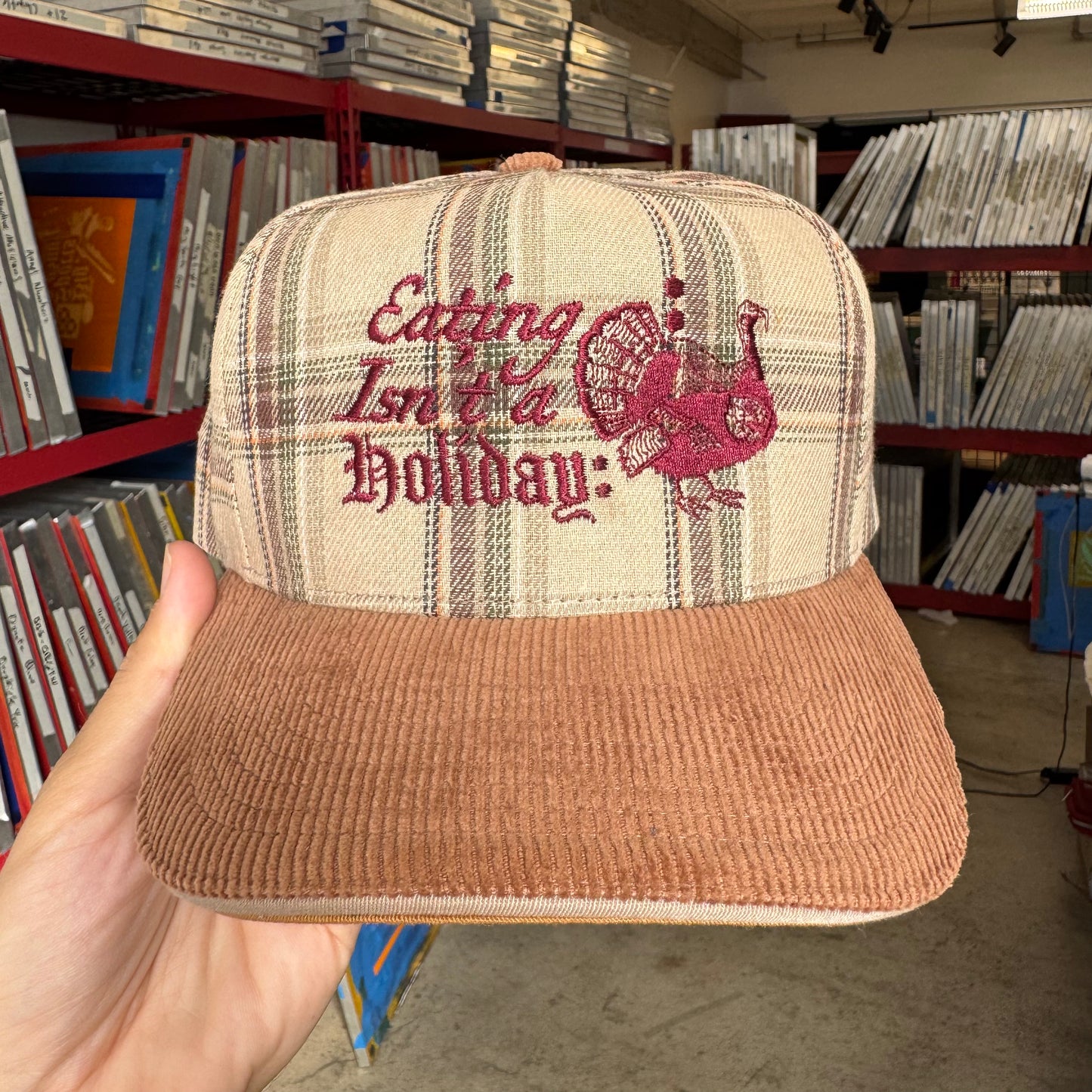 Cap with 'Eating Isn't a Holiday' text and graphic held in front of record store shelves.