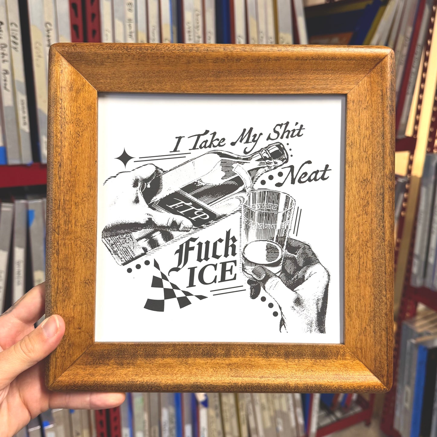 Framed artwork with black and white illustration and text held in front of a bookshelf.