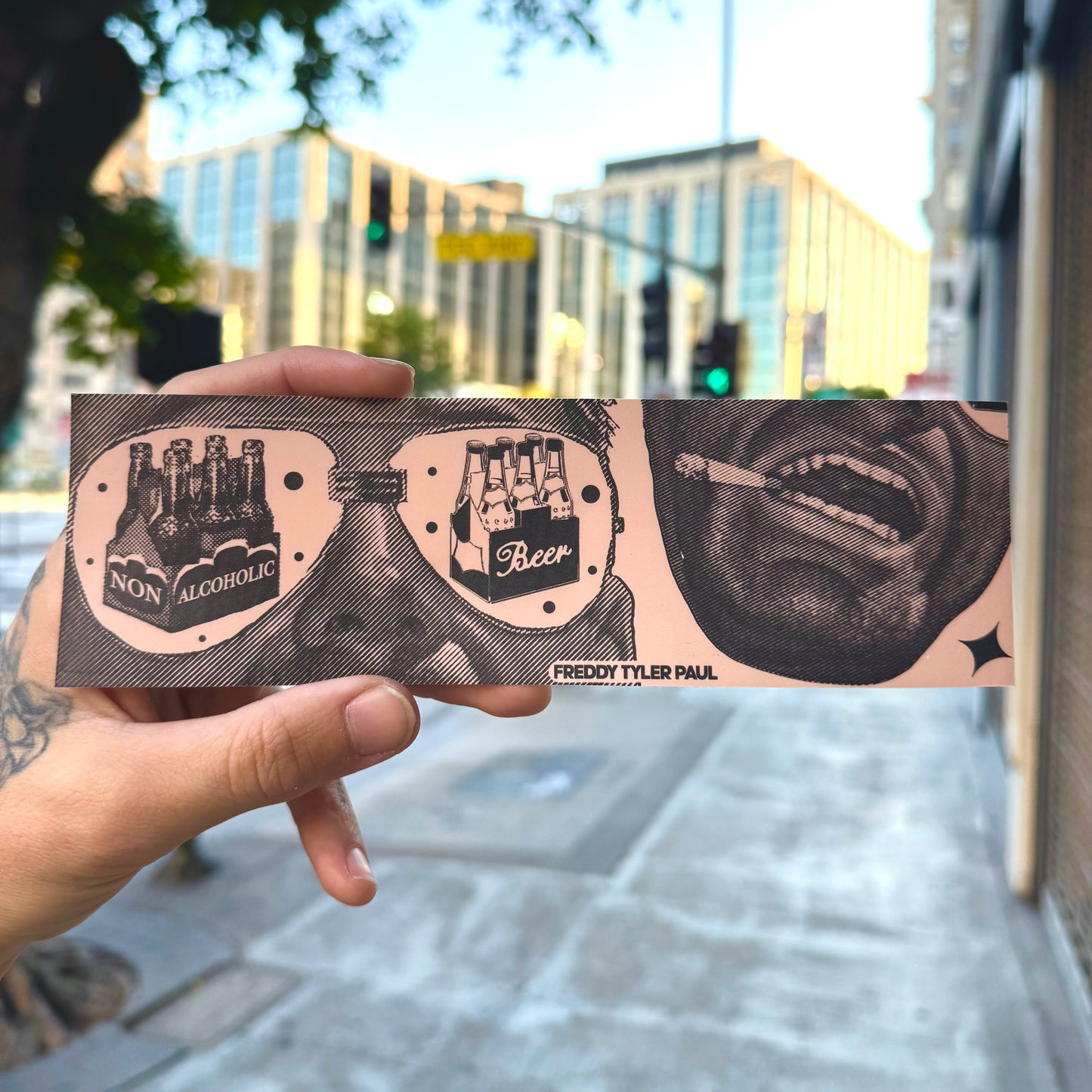 Hand holding a tattoo-style card with graphic designs and text in an urban setting