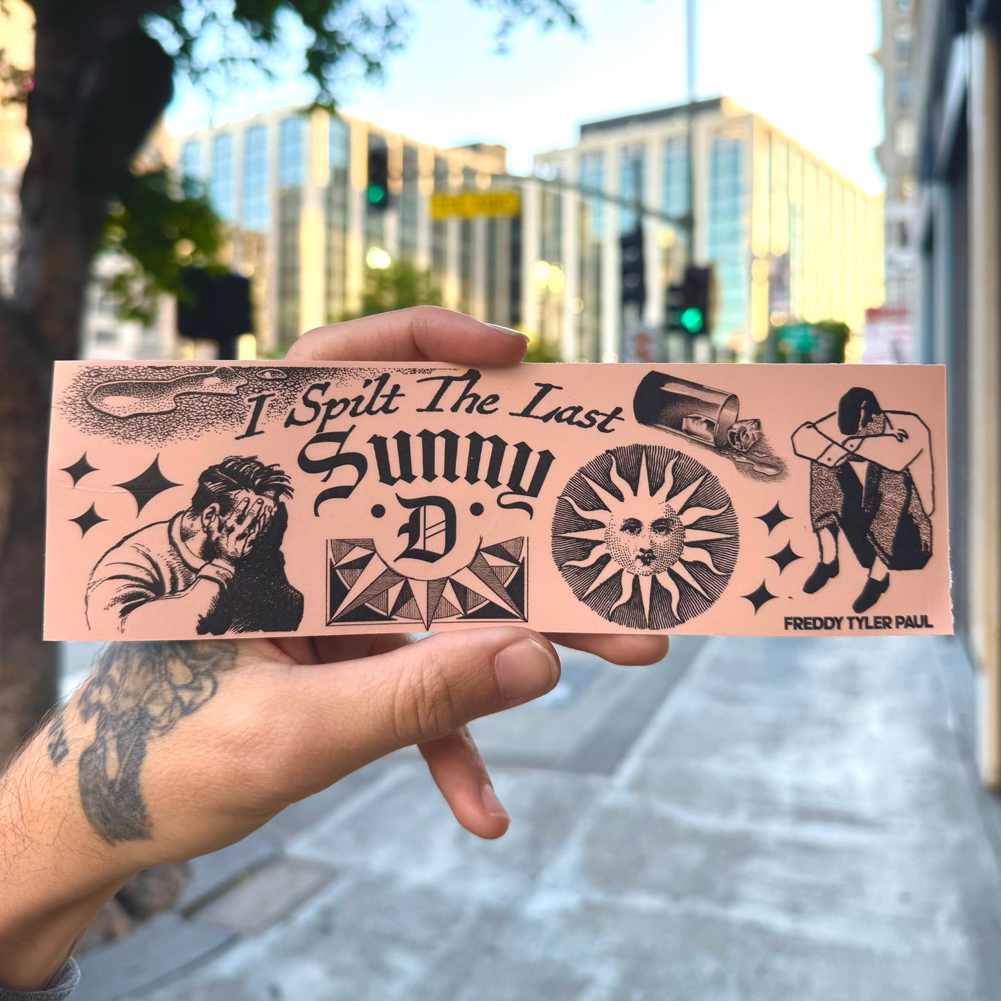 Hand holding a pink bumper sticker with black graphics and text in an urban setting