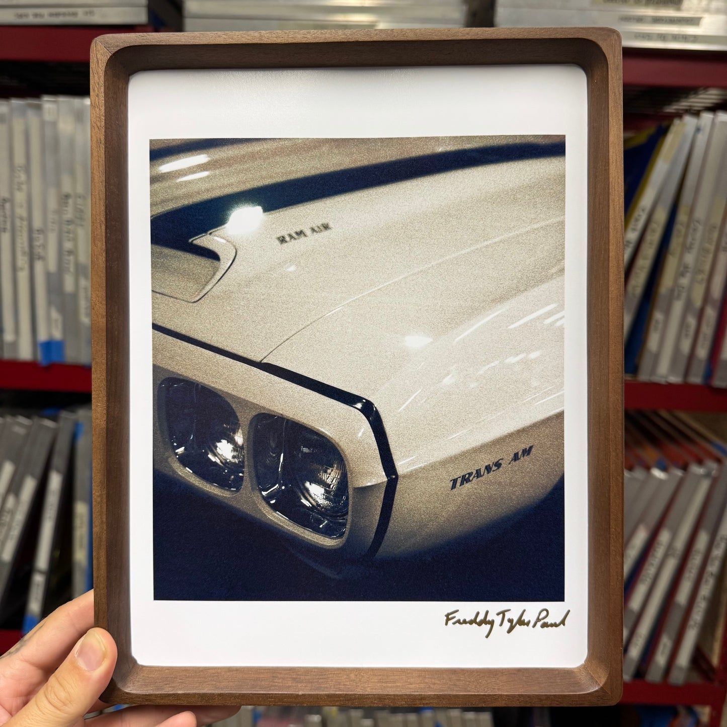 Framed picture of a car's headlight held in front of a bookshelf.