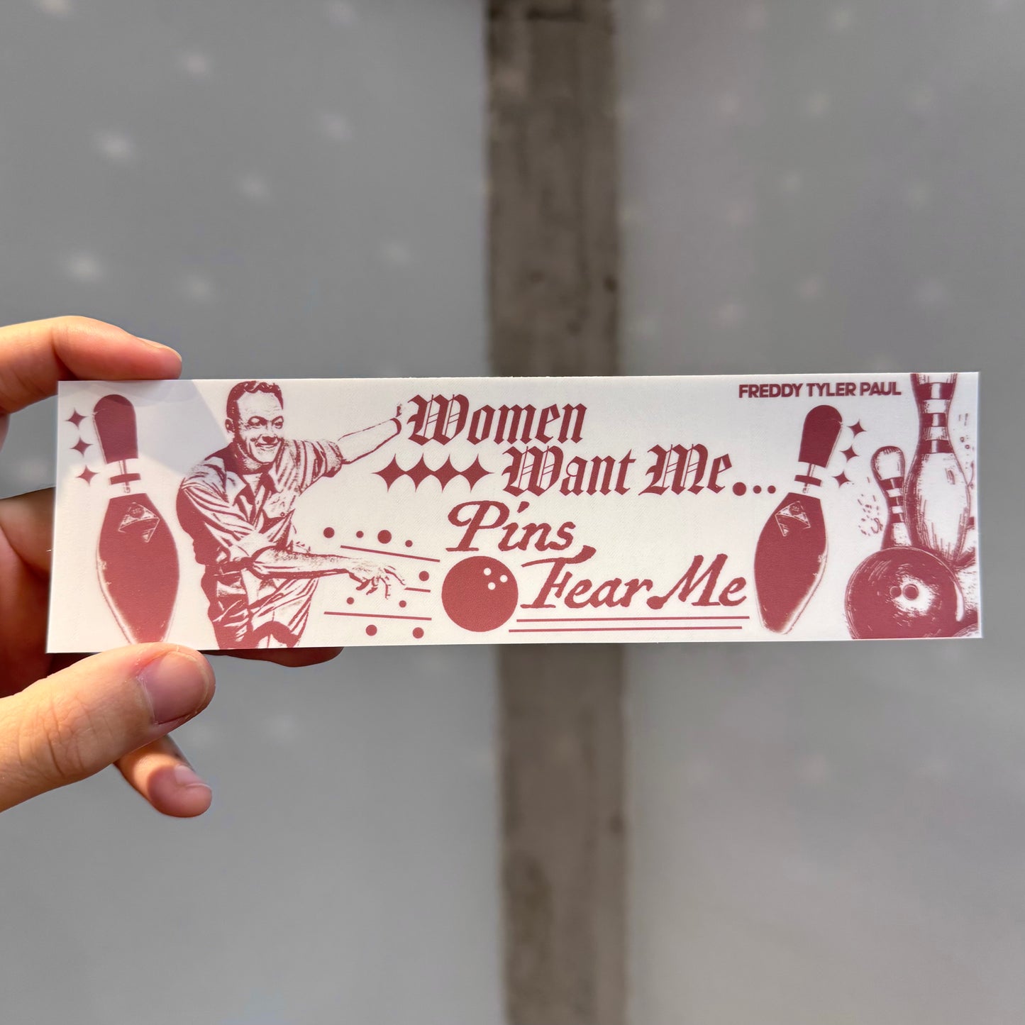 Hand holding a bumper sticker with a humorous bowling design and text.