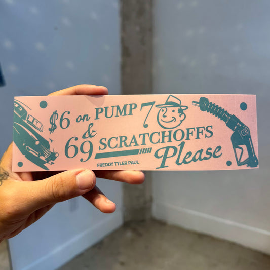 Hand holding a pink scratchoff ticket with text and graphics against a light blue wall.