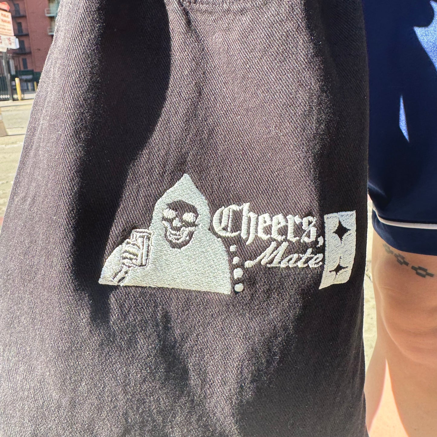 Embroidered logo on a dark fabric with 'Cheers, Mate' text and a skull design.