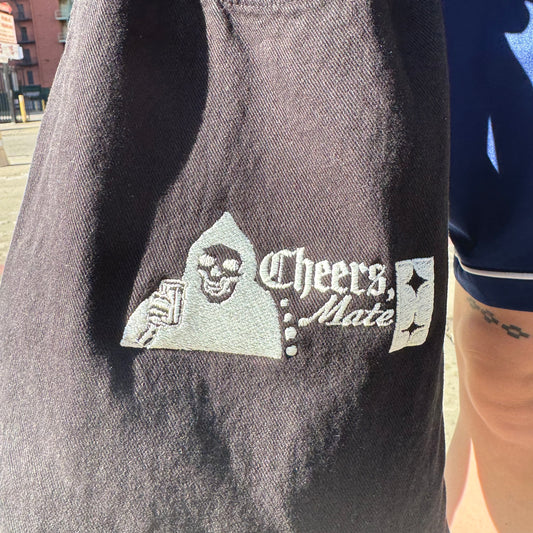 Embroidered logo on a dark fabric with 'Cheers, Mate' text and a skull design.