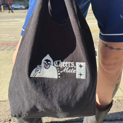 Black tote bag with a graphic design held by a person outdoors.