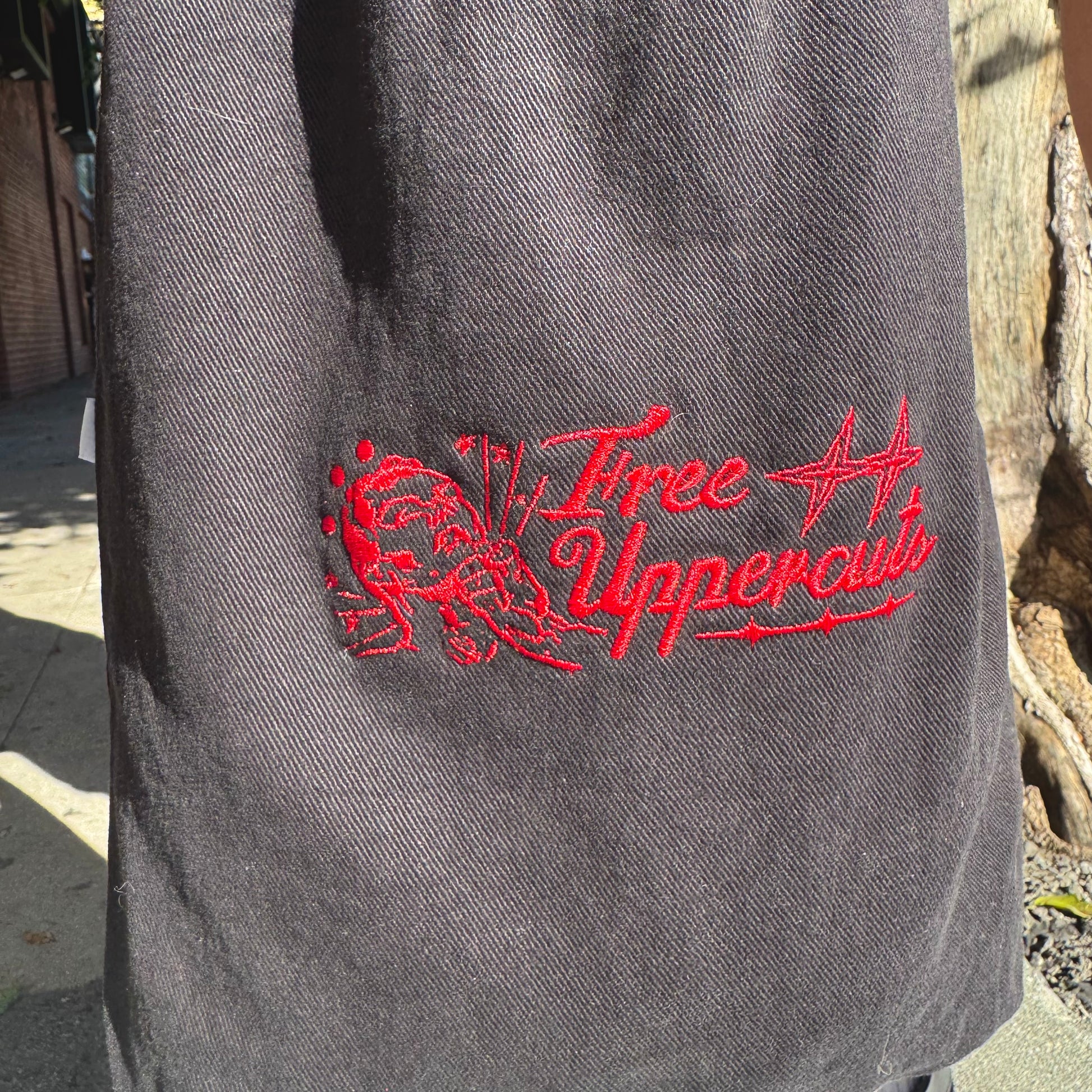 Gray jacket with red 'Three Uppercuts' logo on a blurred outdoor background