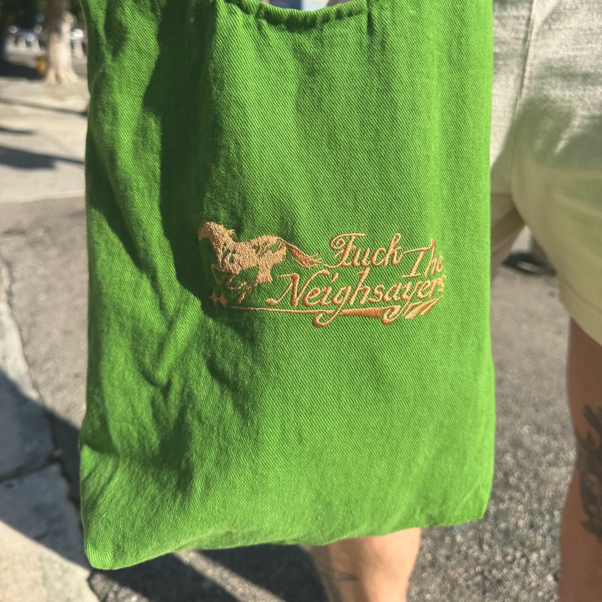 Green bag with embroidered text and design on a person's arm outdoors.