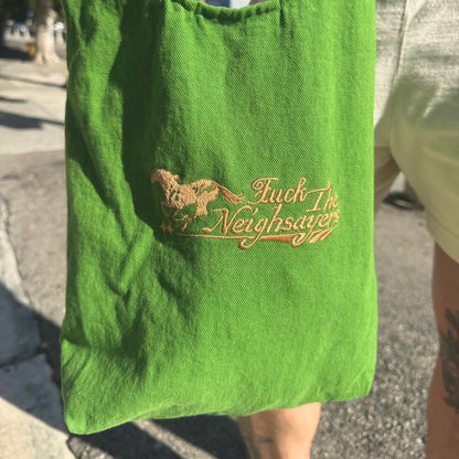 Green bag with embroidered text and design on a person's arm outdoors.