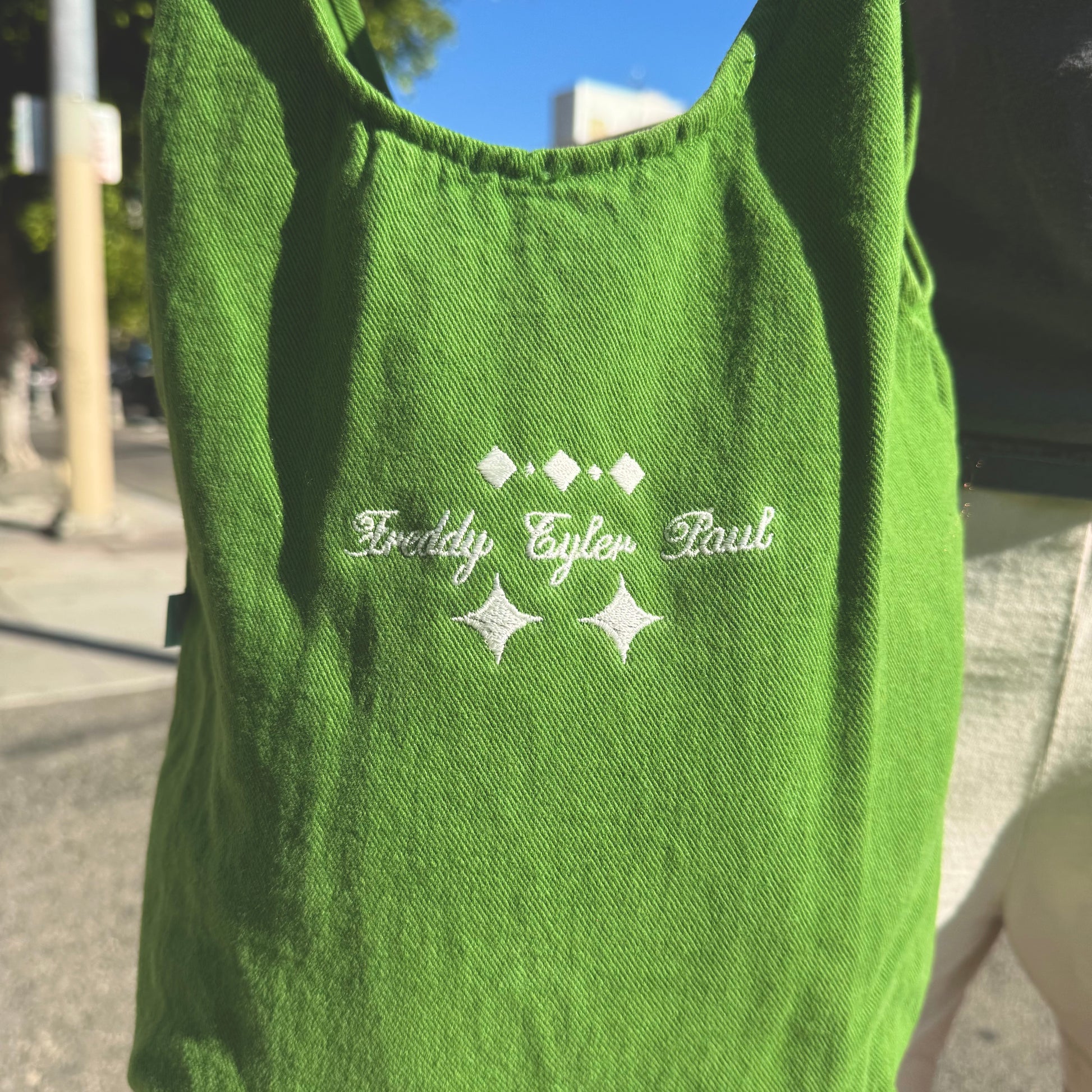 Green tank top with embroidered text and star designs on a blurred street background
