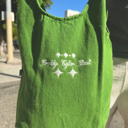Green tank top with embroidered text and star designs on a blurred street background