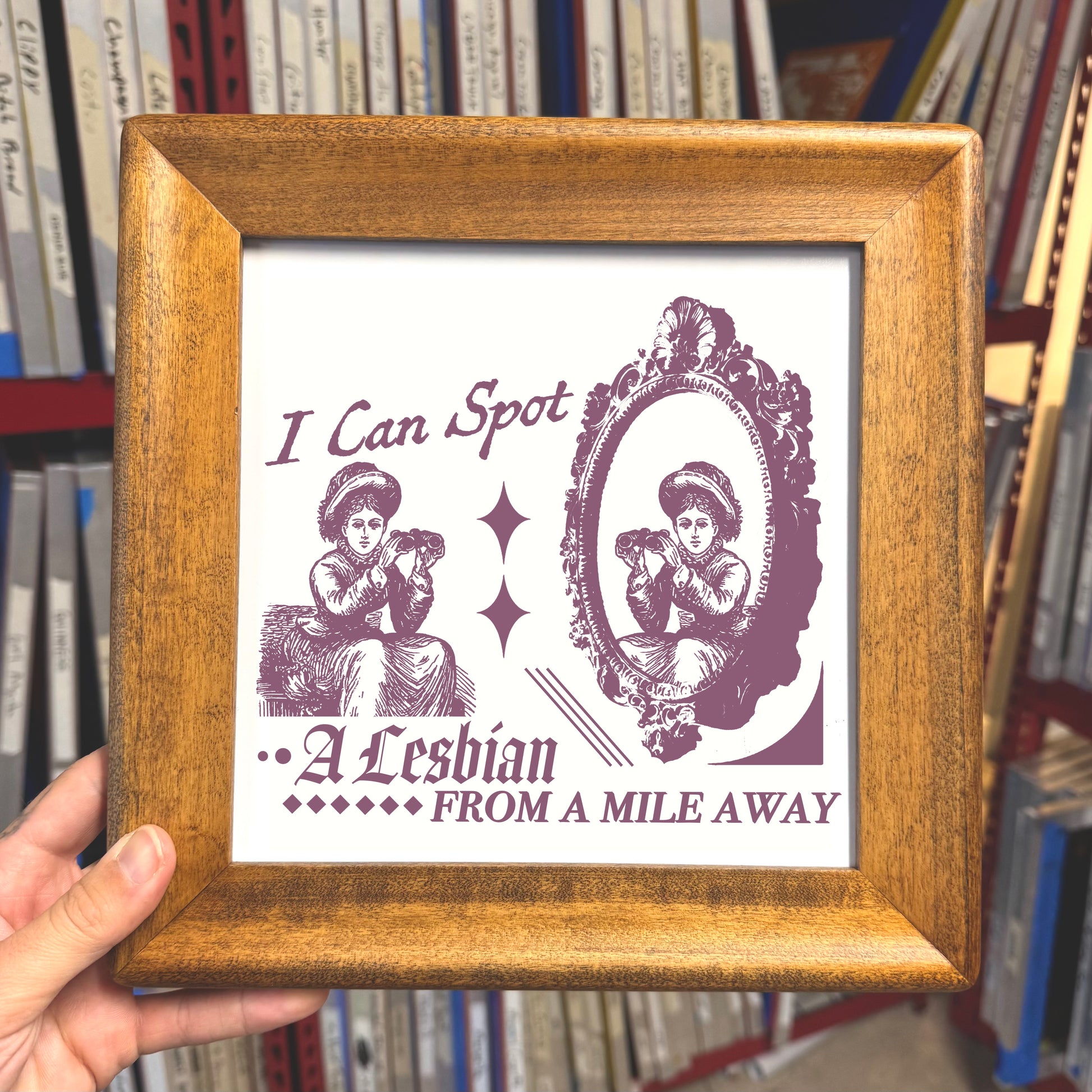 Framed print with text and illustration of a woman, held in front of bookshelves.