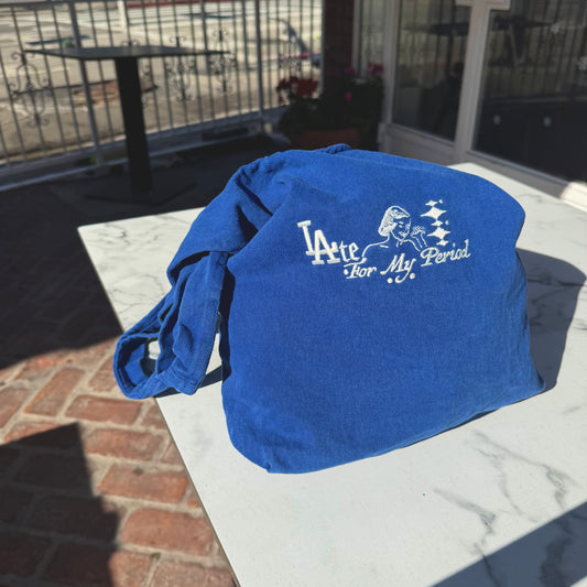 Blue bag with 'Late For My Period' text on a marble surface outdoors
