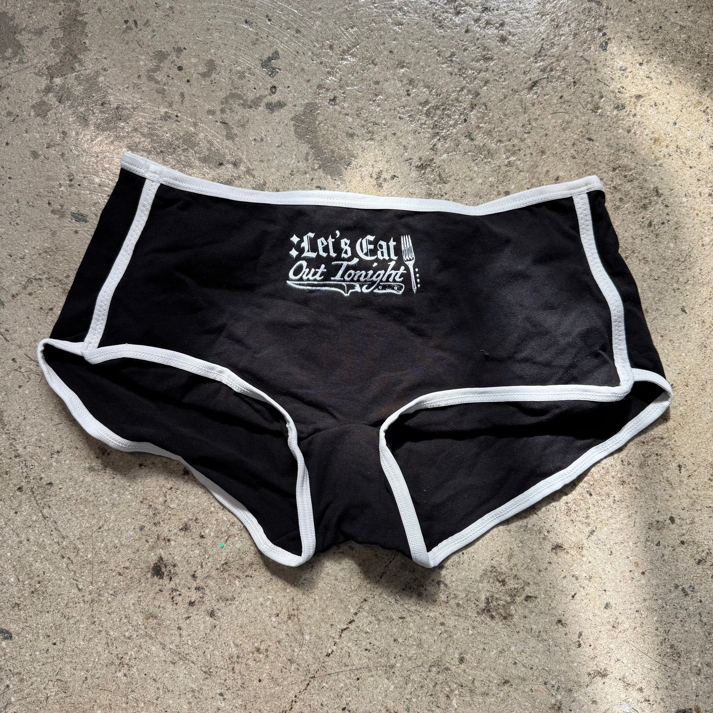 Black underwear with white trim and text on a concrete surface