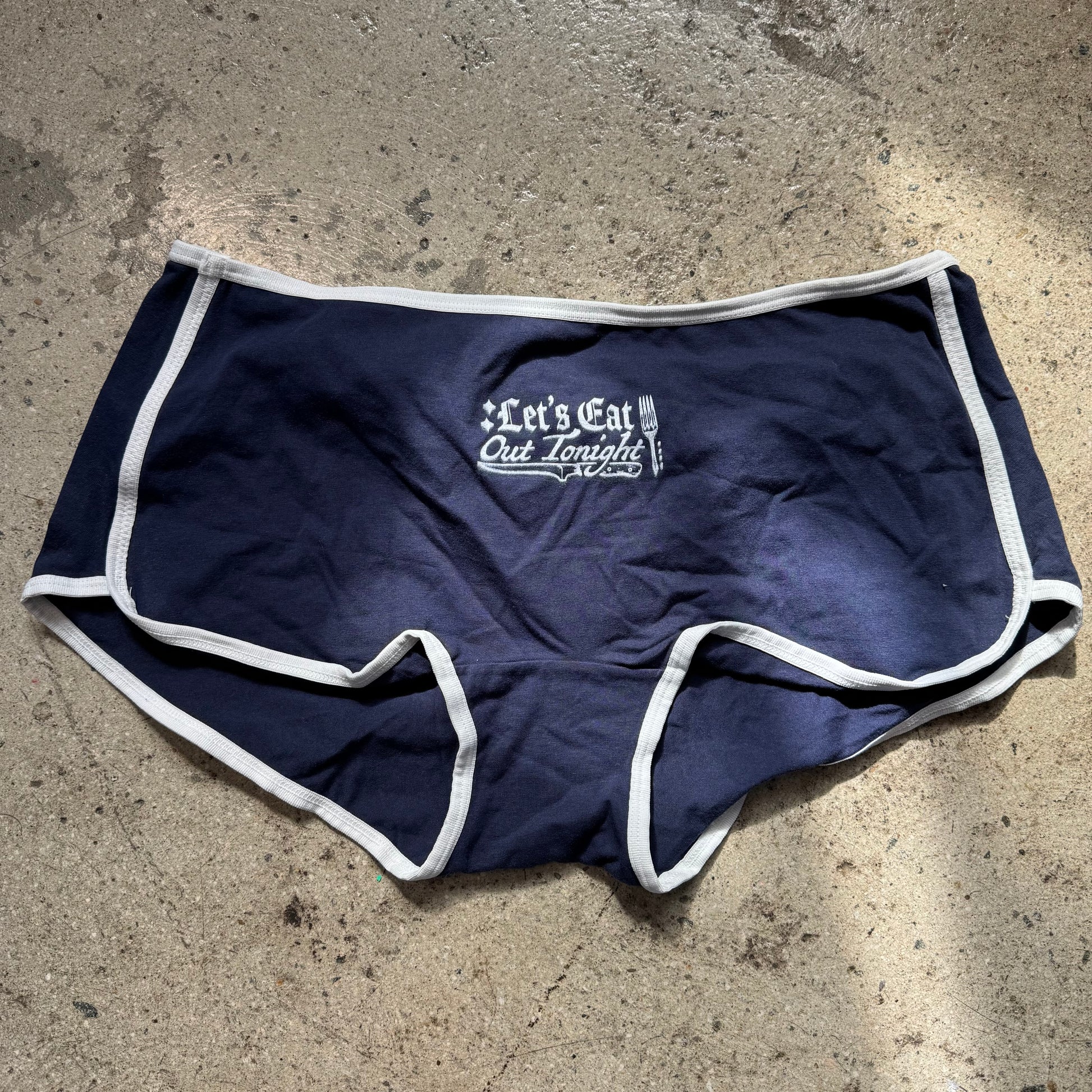Navy blue shorts with white trim on a concrete surface