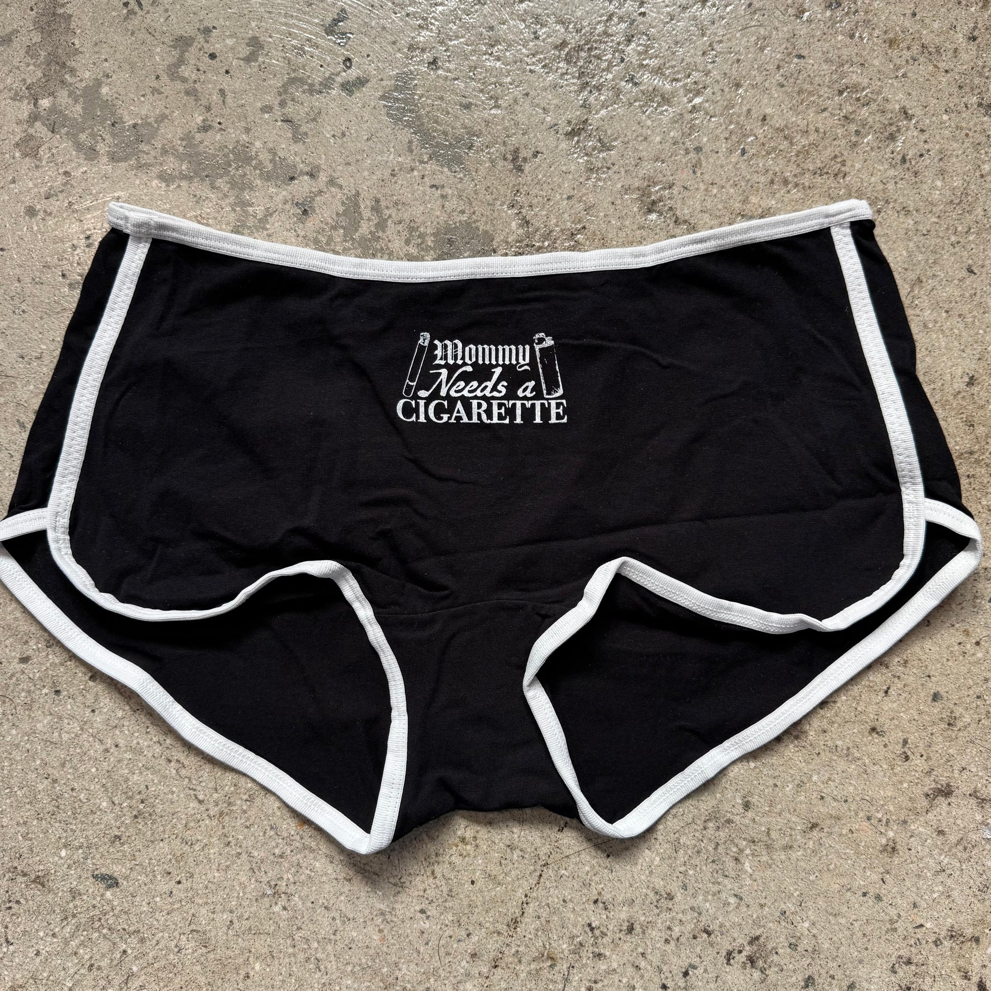Black shorts with white trim and text on a concrete surface