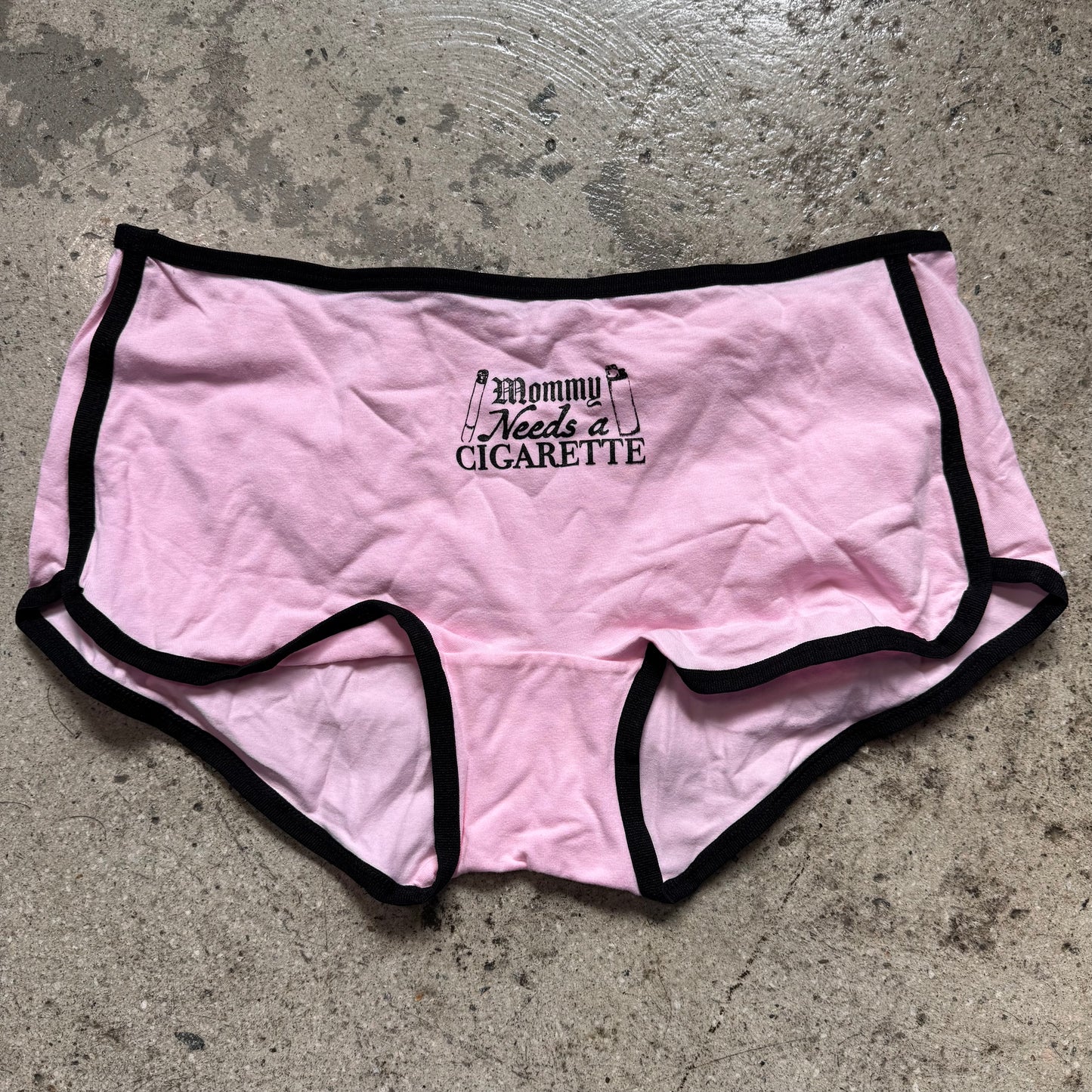 Pink underwear with black trim and text on a concrete floor