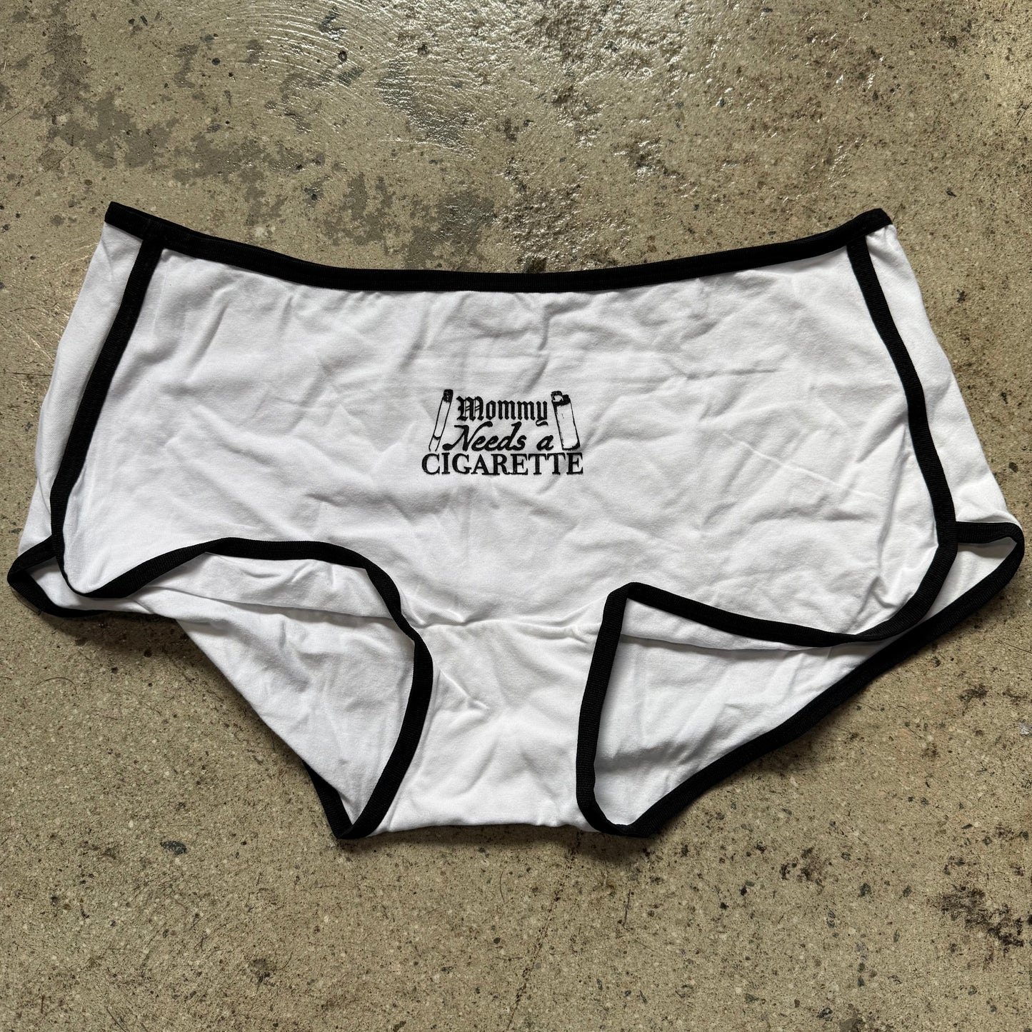 White underwear with black trim and text on a concrete surface