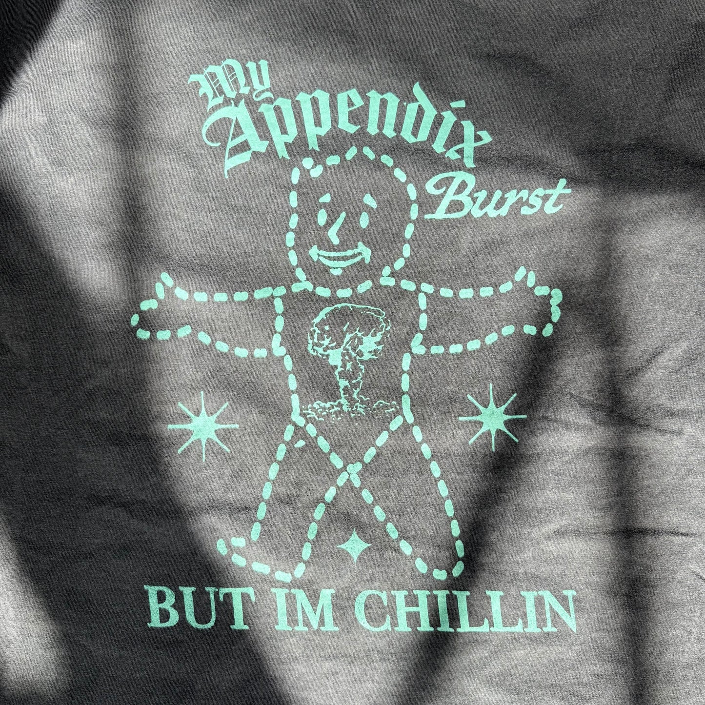 T-shirt with a graphic design and text 'My Appendix Burst, But I'm Chillin' on a dark background