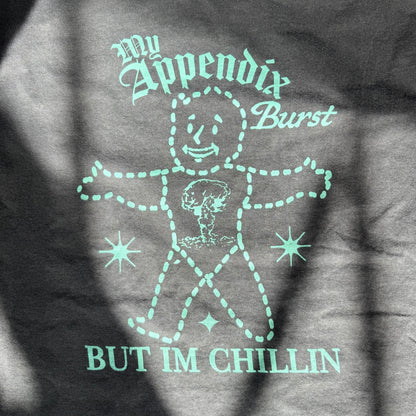 T-shirt with a graphic design and text 'My Appendix Burst, But I'm Chillin' on a dark background
