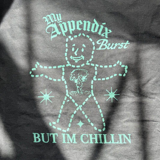 T-shirt with a graphic design and text 'My Appendix Burst, But I'm Chillin' on a dark background