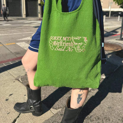 Person holding a green tote bag with text and graphics on a city street.