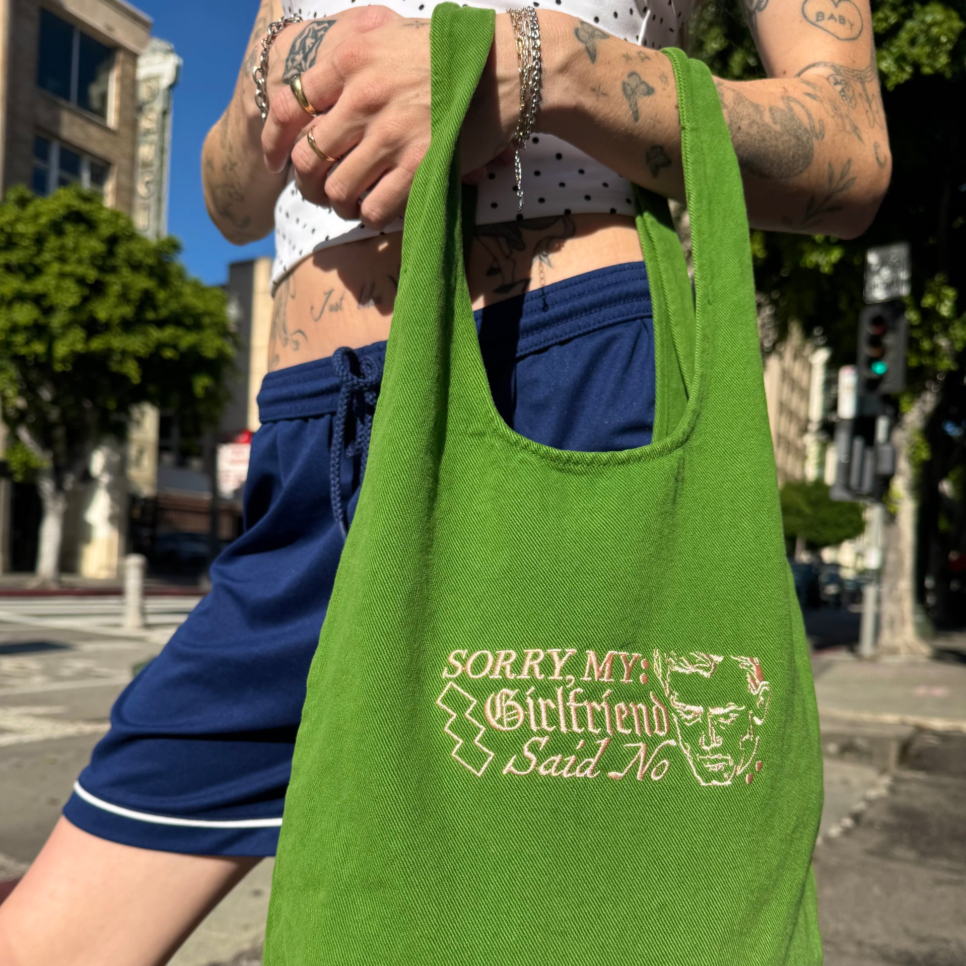 Person holding a green tote bag with text and graphic design on a city street.