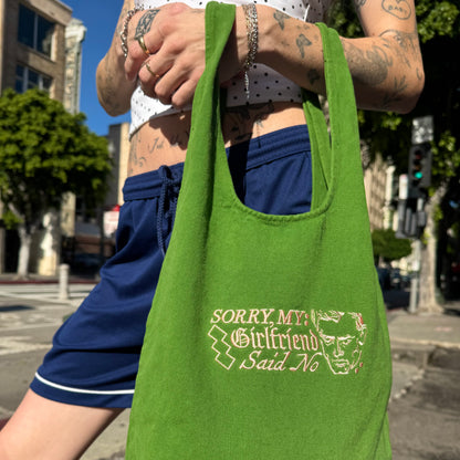 Person holding a green tote bag with text and graphic design on a city street.