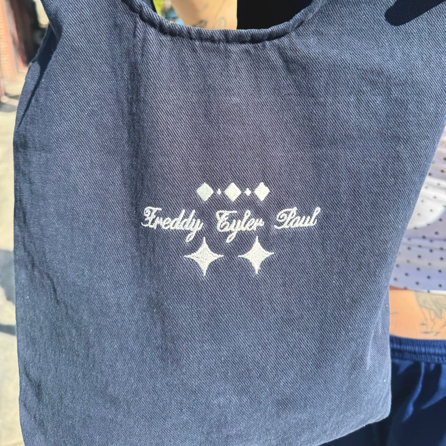 Blue tote bag with embroidered text and star designs on a person wearing it.