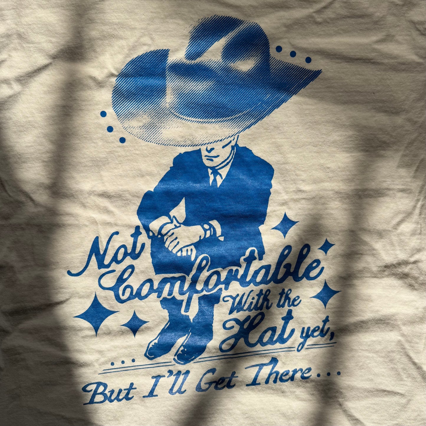 T-shirt with blue graphic of a person wearing a hat and text on a beige background