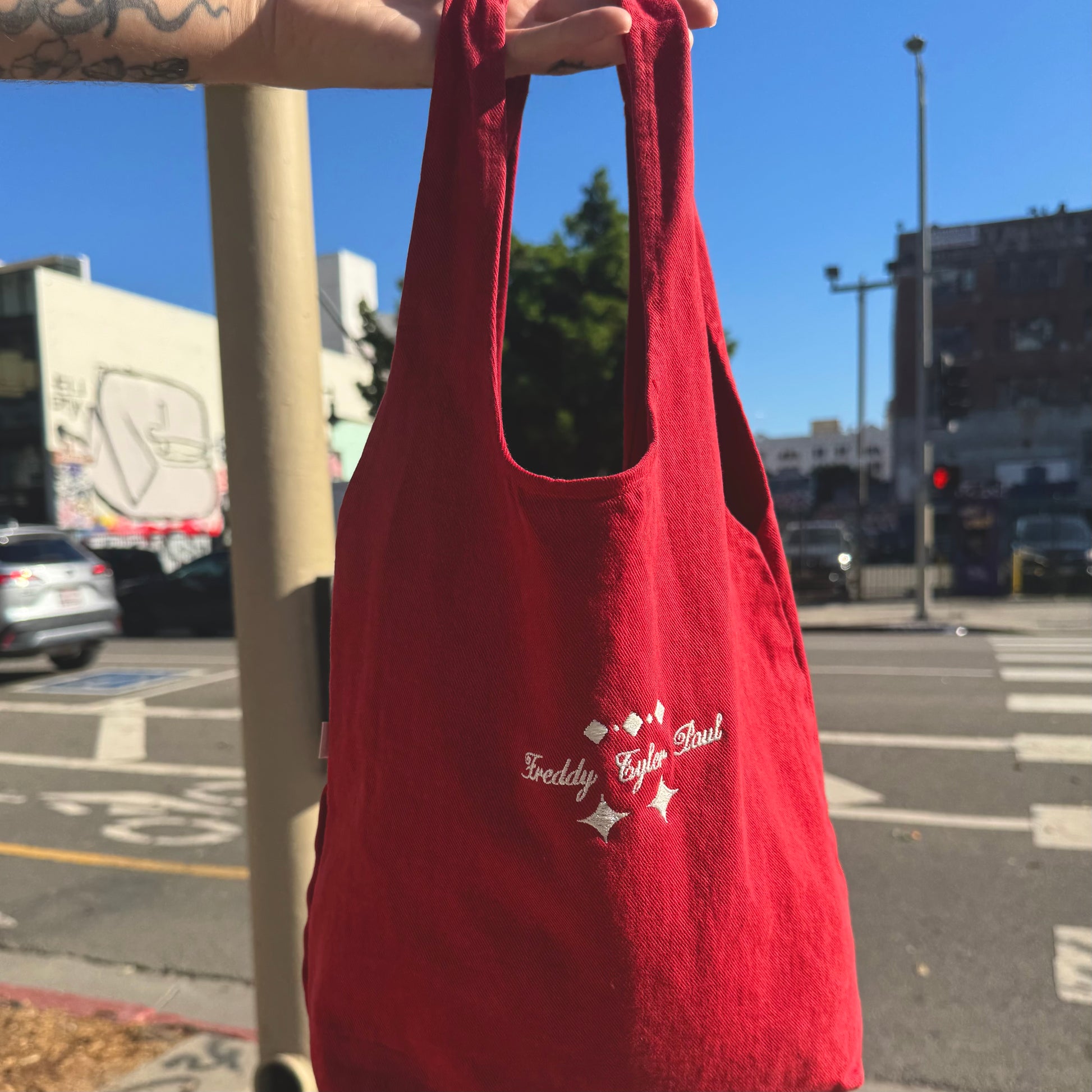 Red tote bag with branding held up against a city street background