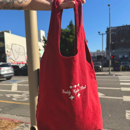 Red tote bag with branding held up against a city street background