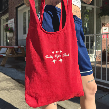 Person holding a red tote bag with branding outdoors