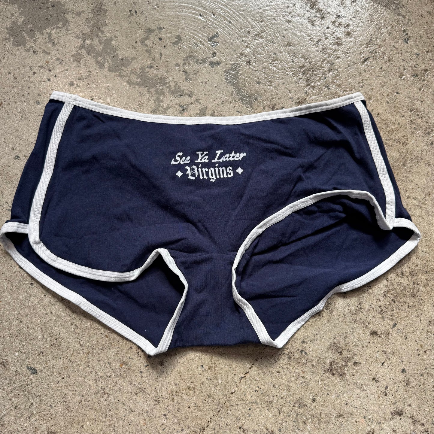 Navy blue shorts with white trim and text on a concrete surface