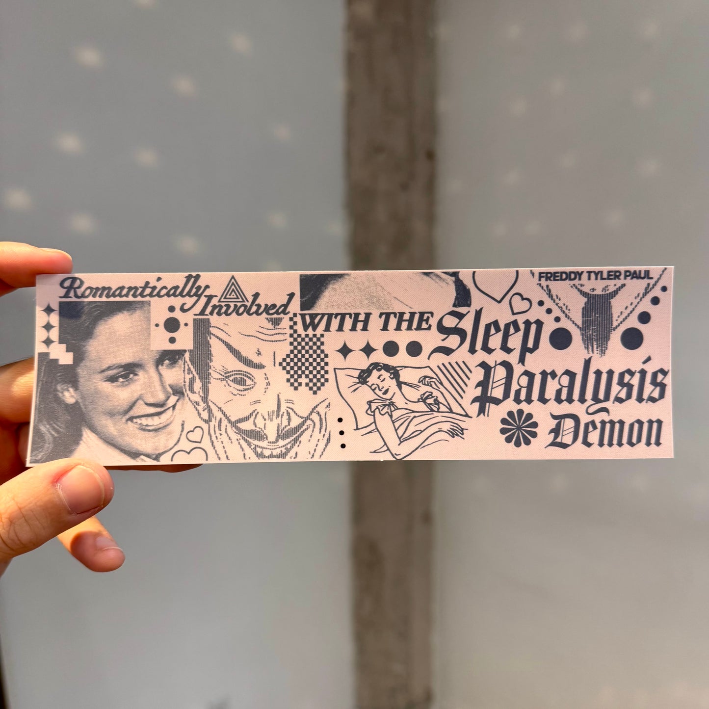 Card with black and white illustration and text held by a hand against a gray background