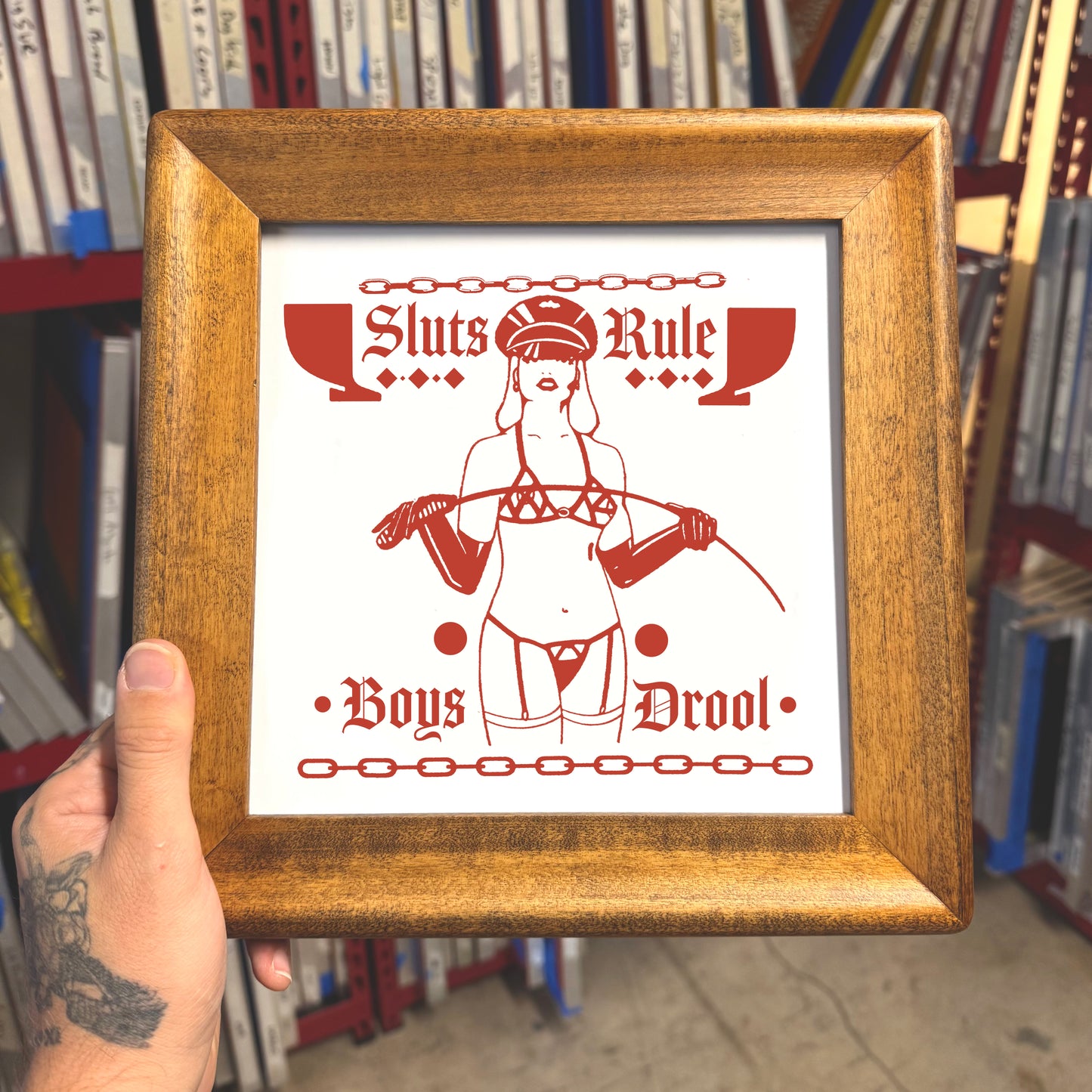 Framed poster with red and white design held in front of a bookshelf.