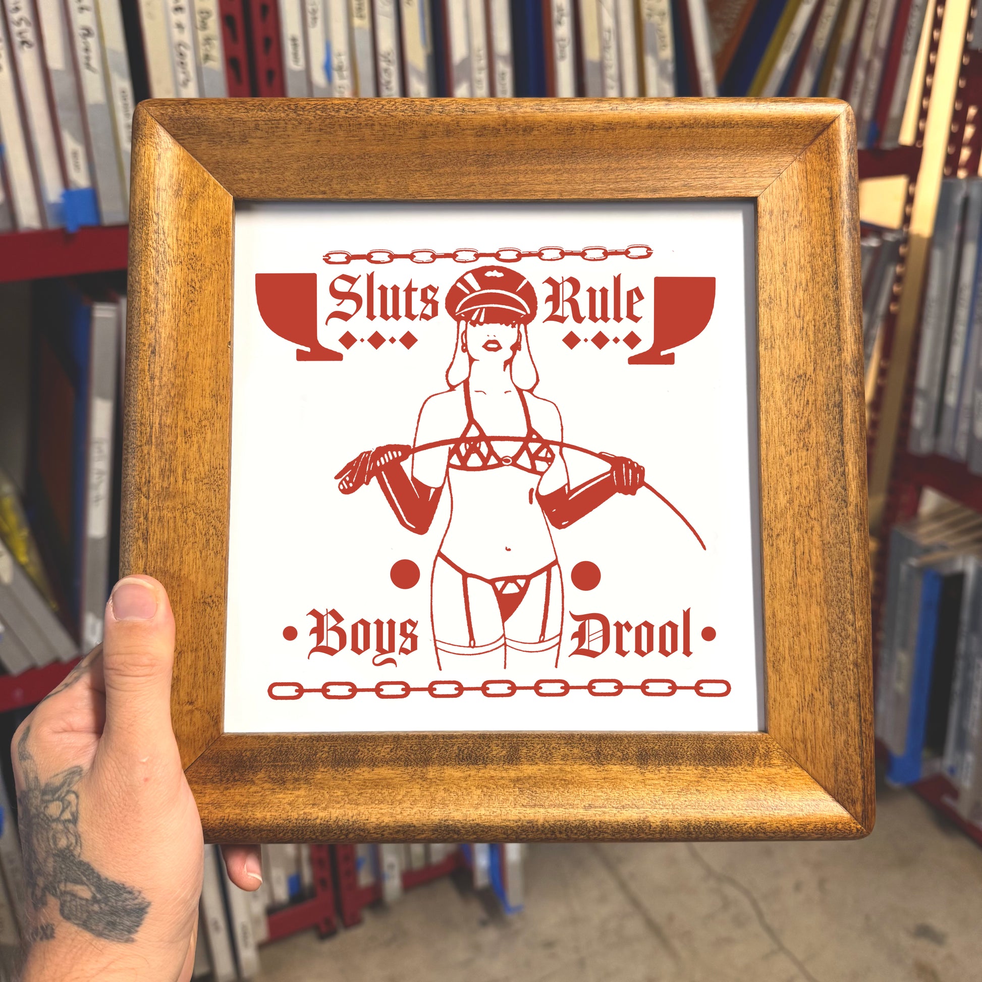 Framed poster with red and white design held in front of a bookshelf.