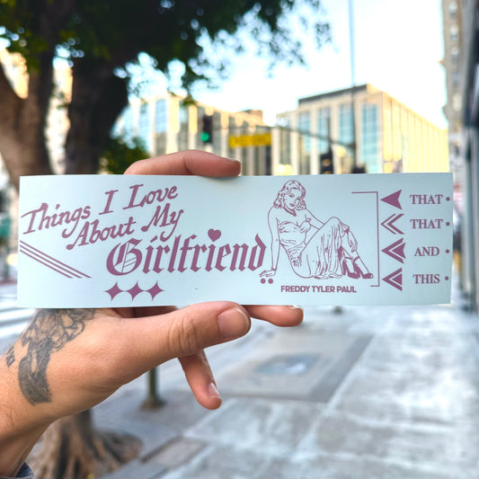 Hand holding a bumper sticker with text and a graphic design outdoors.