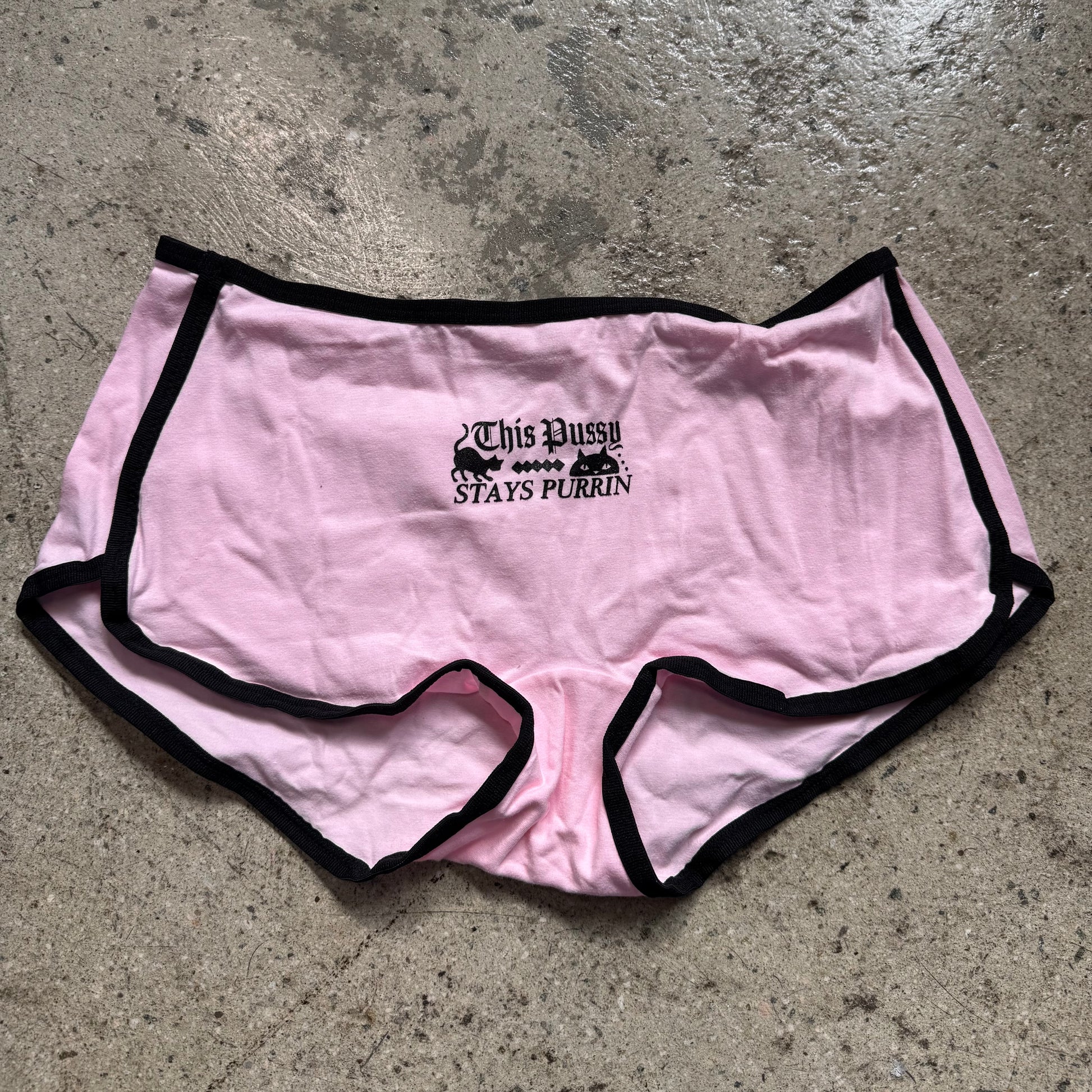 Pink shorts with black text on a concrete floor