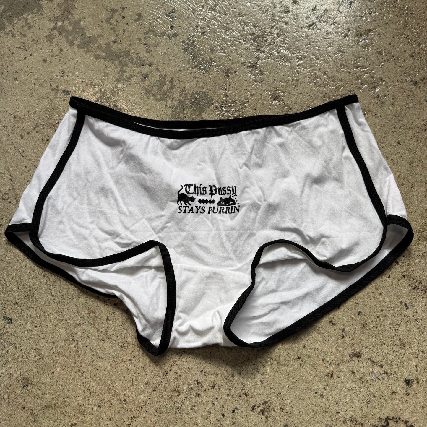 White underwear with black trim on a concrete floor
