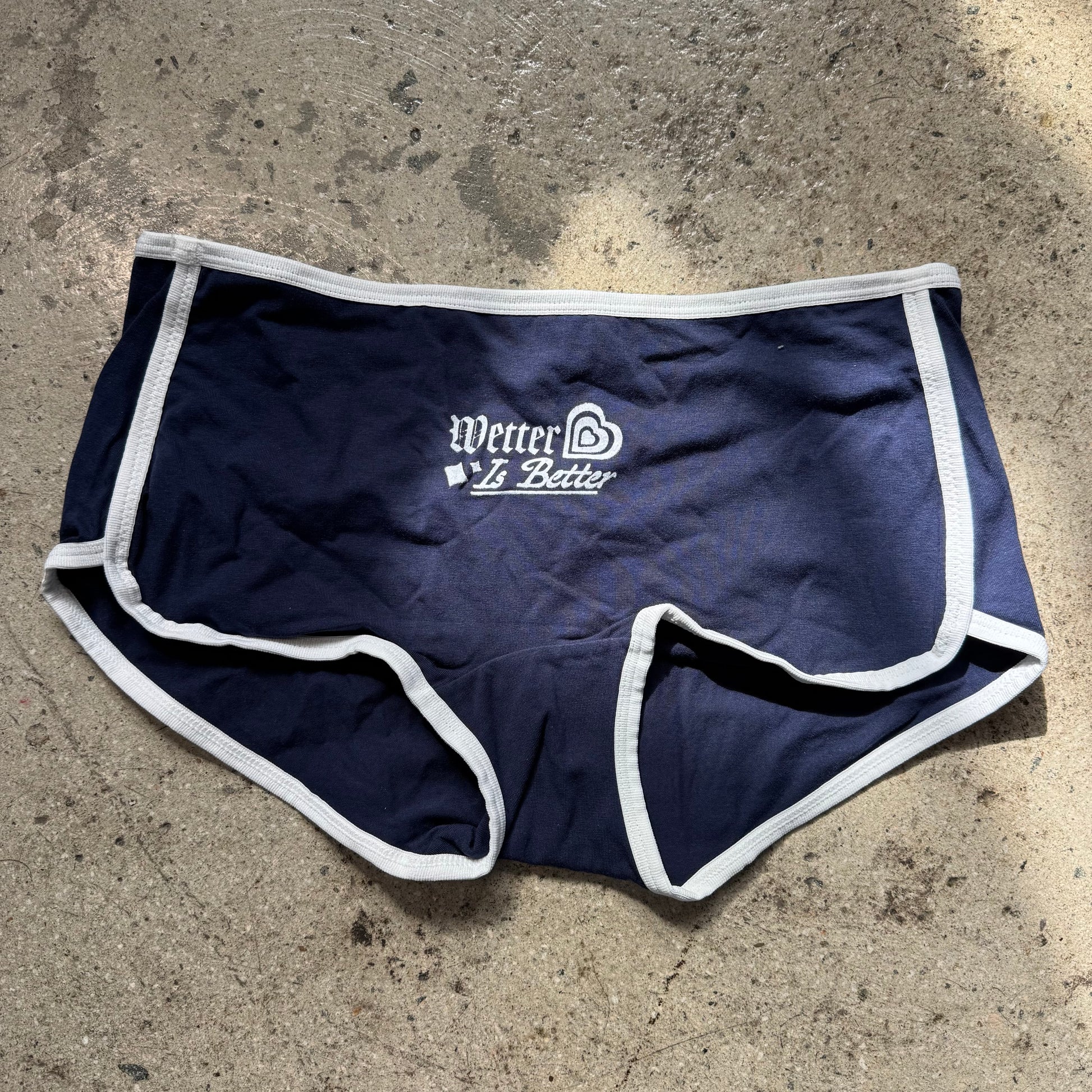 Navy blue athletic shorts with white trim on a concrete surface