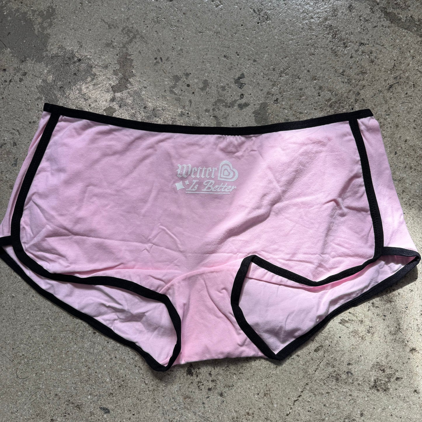 Pink underwear with black trim on a gray concrete surface