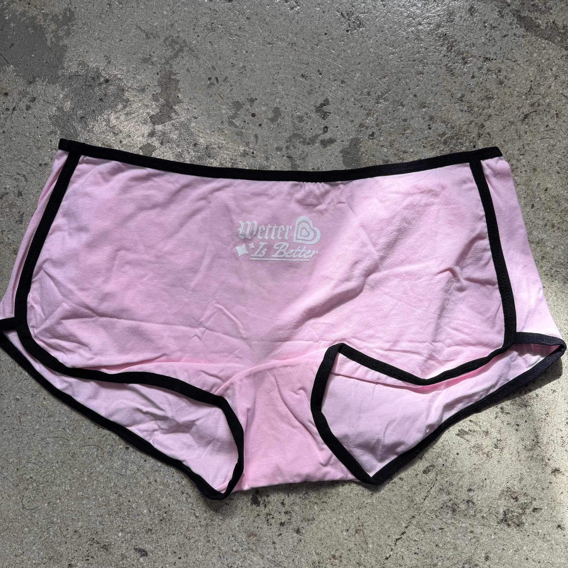 Pink underwear with black trim on a gray concrete surface