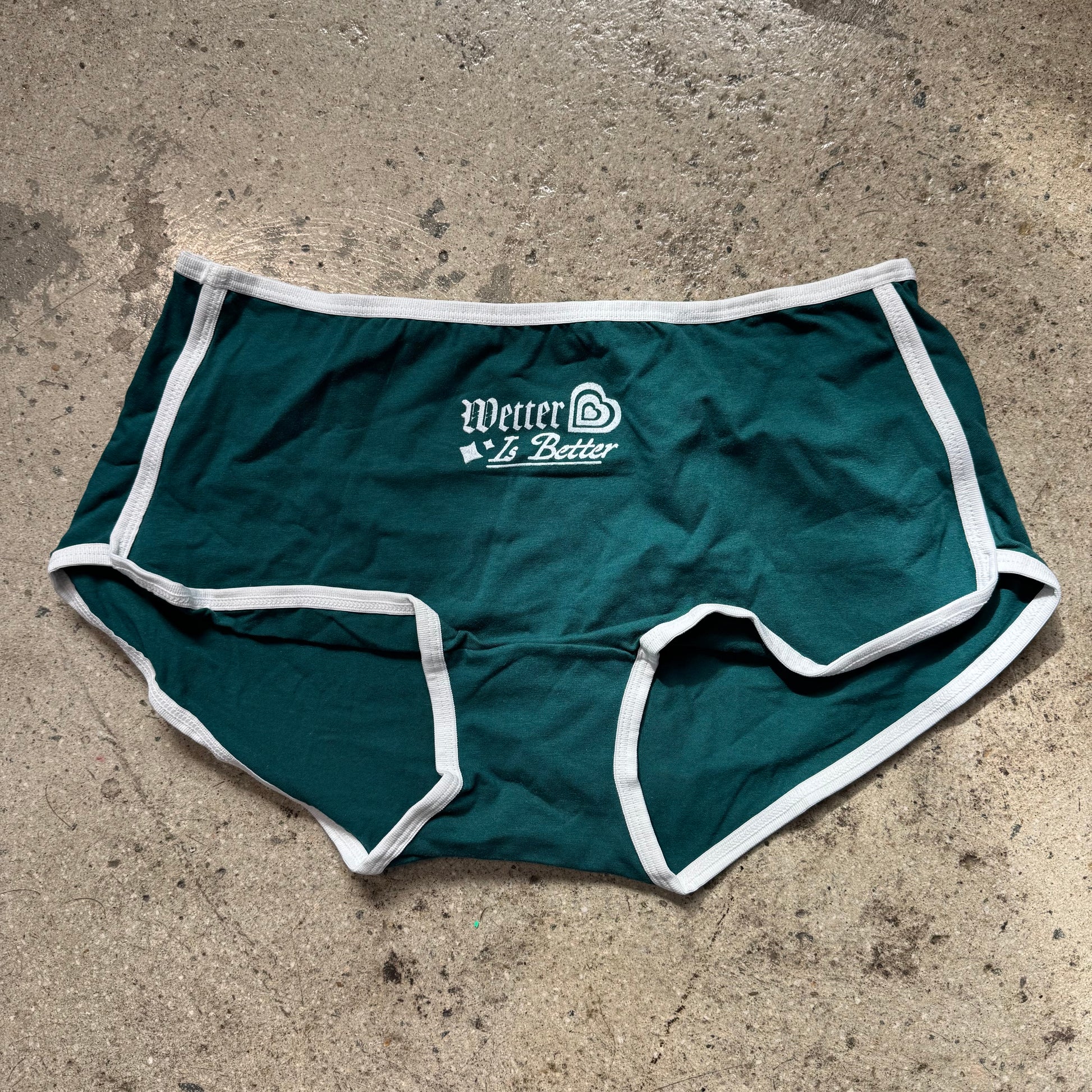 Green athletic shorts with white trim on a concrete surface