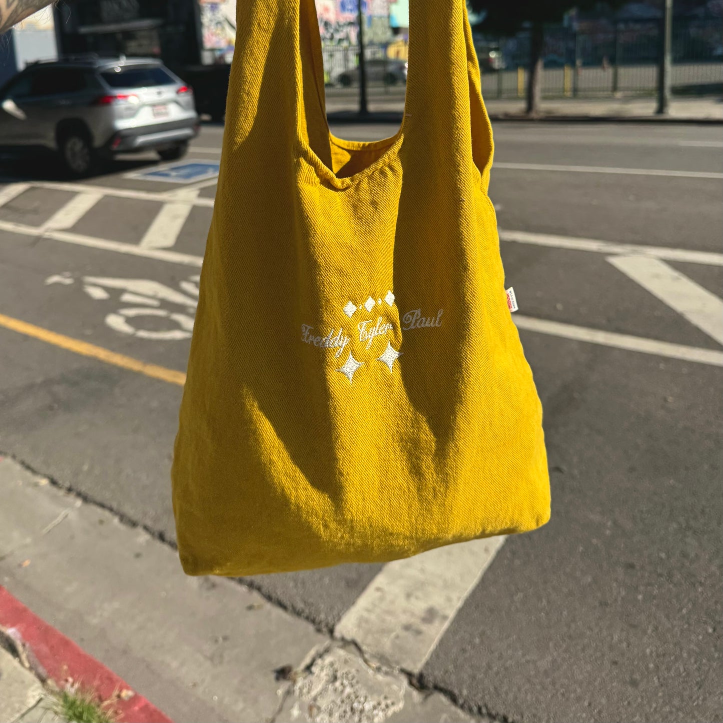 Yellow tote bag with branding held up on a street
