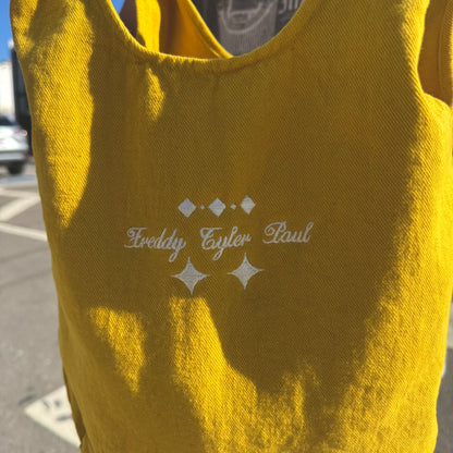 Yellow sleeveless top with 'Freddy Tyler Paul' branding on a blurred street background